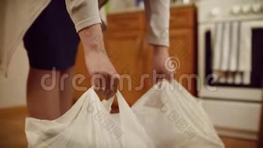 女人把包裹放在地板上。 女人的特写`双手放在地上沉重的食物袋里。 家庭食品采购